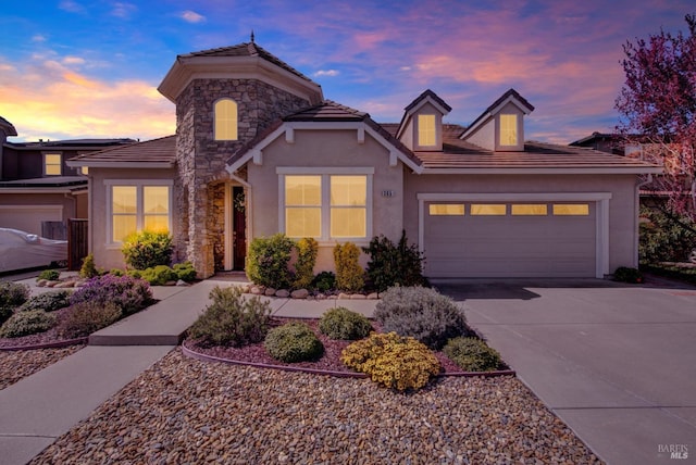 view of front of home featuring stucco siding, stone siding, an attached garage, and a tile roof