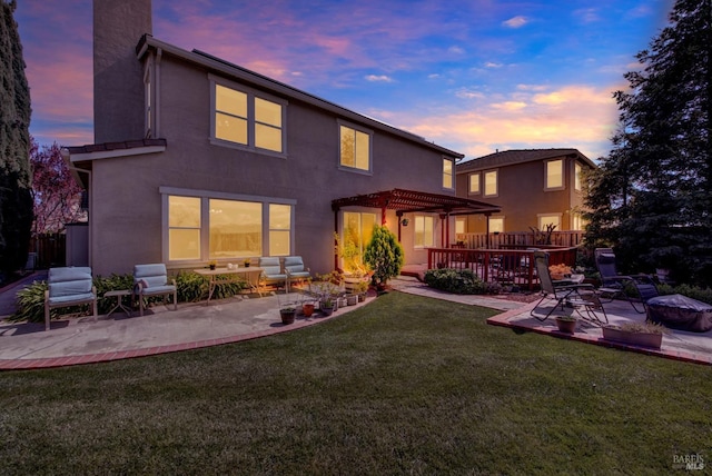 back of property at dusk with stucco siding, a pergola, a patio, a yard, and a chimney