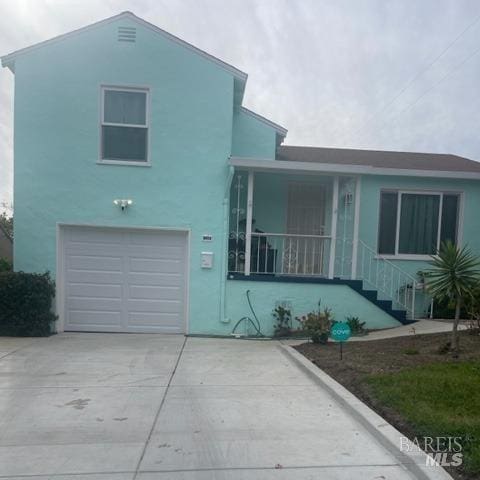 split level home with a porch, a garage, driveway, and stucco siding