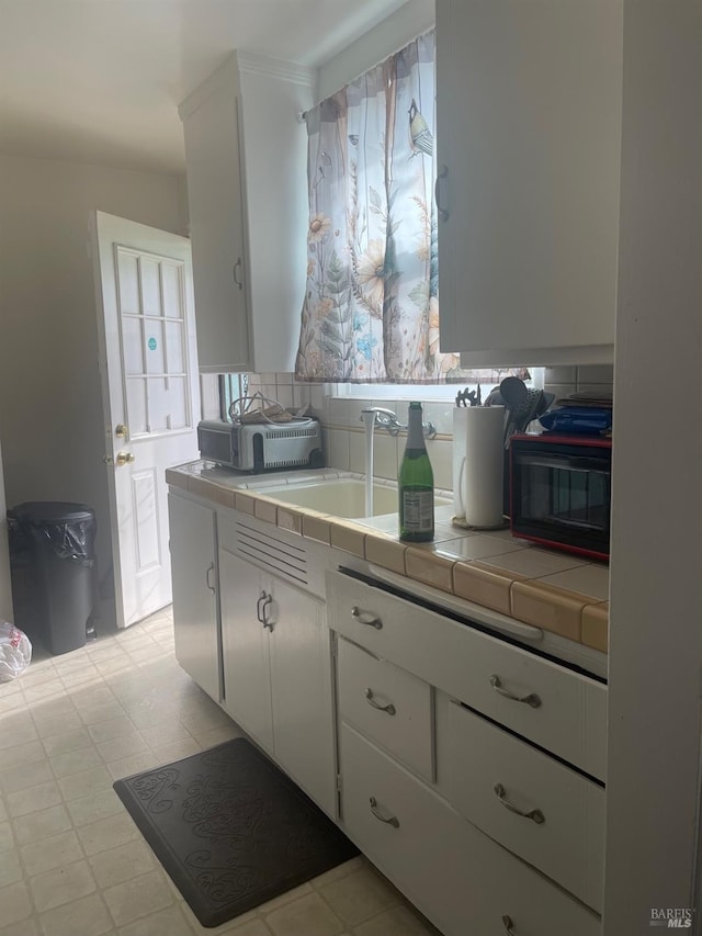 kitchen featuring tile countertops, tasteful backsplash, white cabinets, and a sink