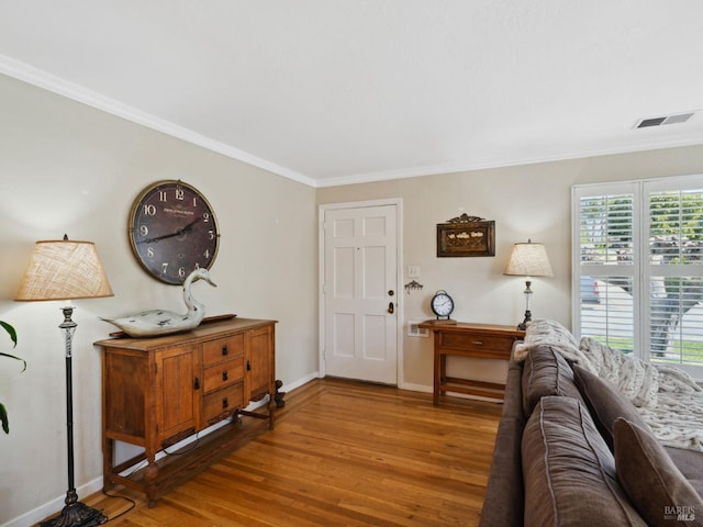living area with crown molding, wood finished floors, visible vents, and baseboards