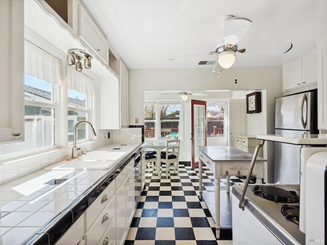 kitchen with tile countertops, a ceiling fan, freestanding refrigerator, a sink, and dark floors