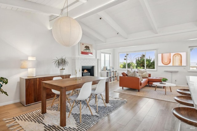 dining area featuring baseboards, a fireplace, light wood-style flooring, and vaulted ceiling with beams