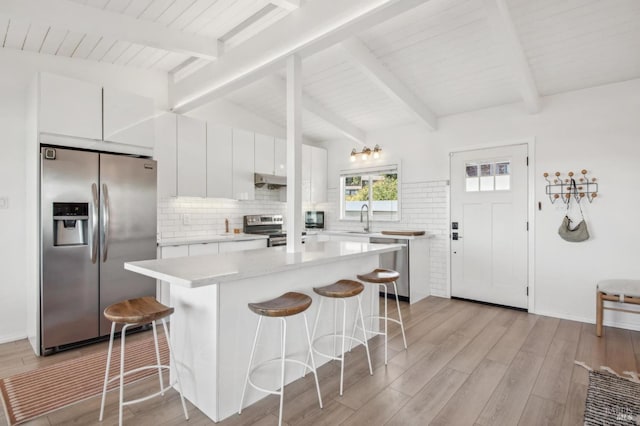 kitchen with vaulted ceiling with beams, a breakfast bar area, light countertops, appliances with stainless steel finishes, and a sink