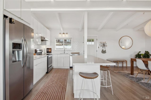 kitchen with a breakfast bar, decorative backsplash, light wood finished floors, and appliances with stainless steel finishes
