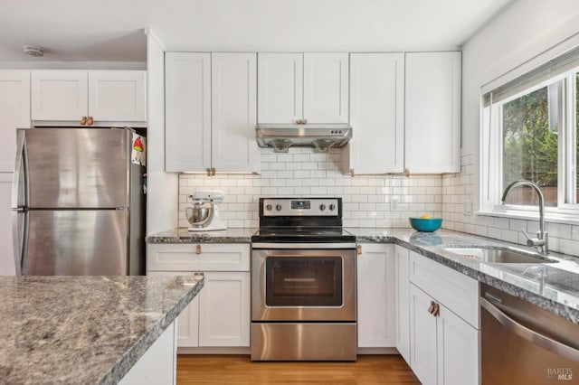 kitchen with a sink, stainless steel appliances, under cabinet range hood, white cabinetry, and tasteful backsplash