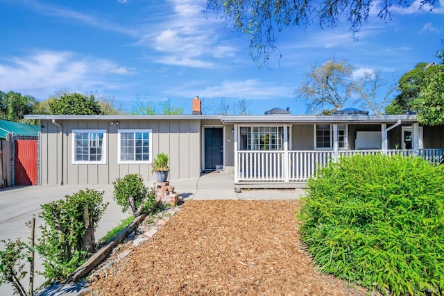 ranch-style home with board and batten siding, fence, covered porch, and a chimney