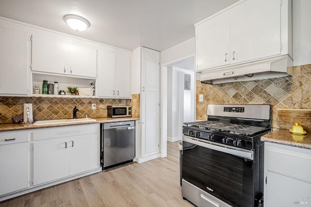 kitchen with under cabinet range hood, stainless steel appliances, decorative backsplash, and a sink