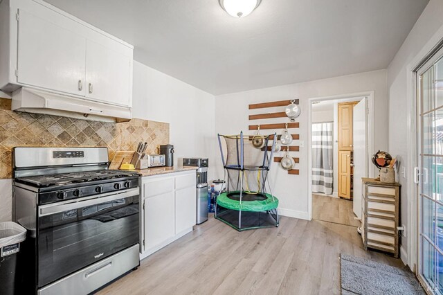 kitchen with light wood-style flooring, under cabinet range hood, stainless steel gas range, and white cabinetry