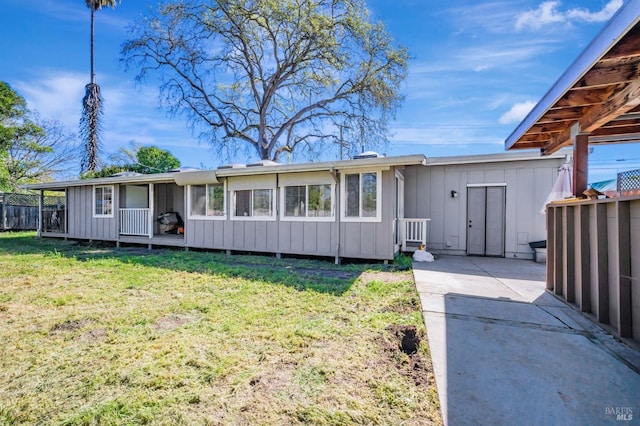 back of property with board and batten siding, a lawn, and fence