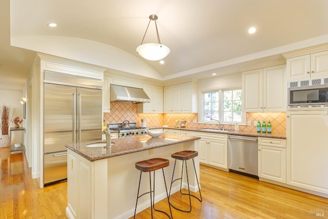 kitchen with built in appliances, light wood-style flooring, wall chimney exhaust hood, and vaulted ceiling