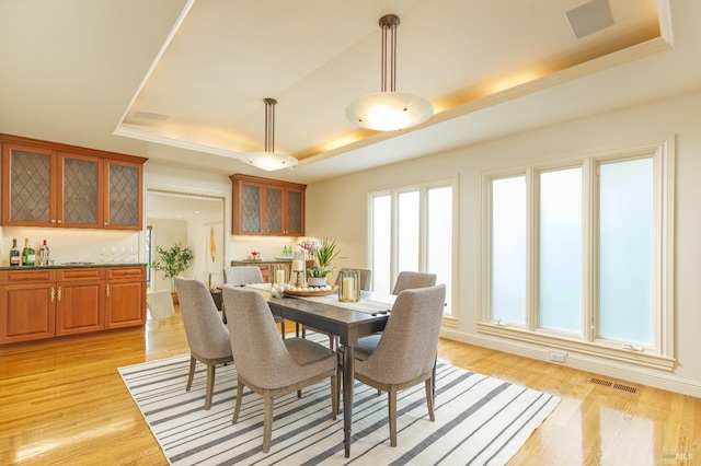 dining area with a raised ceiling, a dry bar, visible vents, and light wood finished floors