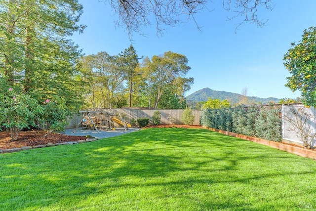 view of yard featuring a playground, a fenced backyard, and a mountain view