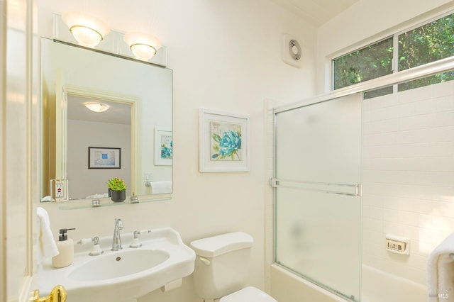 full bathroom featuring toilet, bath / shower combo with glass door, and a sink