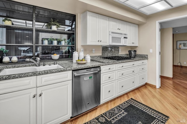kitchen featuring white microwave, white cabinetry, light wood-style flooring, a sink, and stainless steel dishwasher
