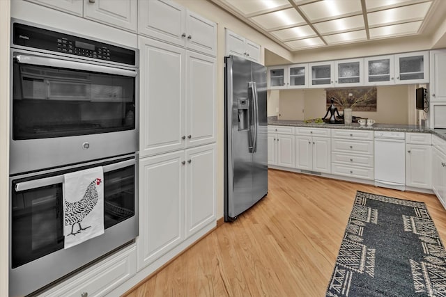 kitchen with light wood finished floors, glass insert cabinets, light stone counters, white cabinets, and stainless steel appliances