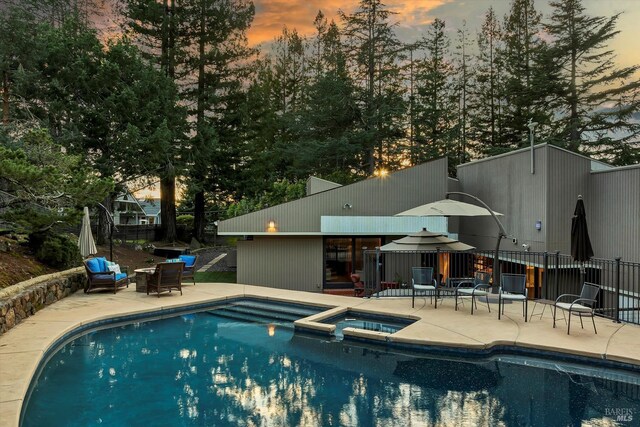 pool at dusk with a patio, a pool with connected hot tub, and fence