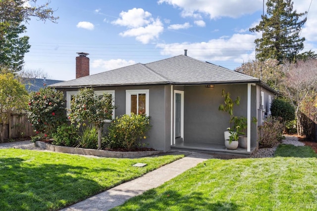 rear view of property with fence, roof with shingles, stucco siding, a lawn, and a chimney