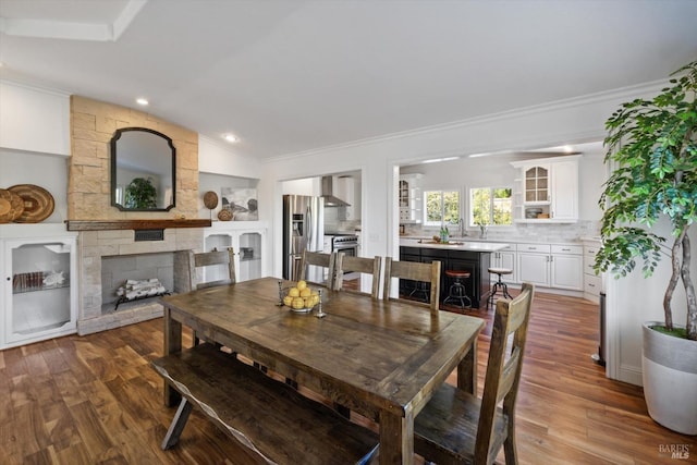dining area with a stone fireplace, wood finished floors, crown molding, and vaulted ceiling