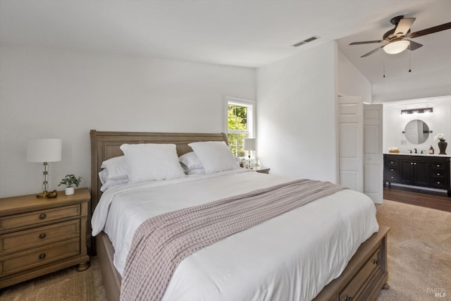 carpeted bedroom with a ceiling fan, visible vents, lofted ceiling, and ensuite bathroom