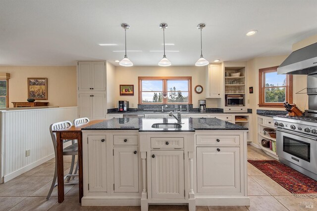 kitchen featuring high end stainless steel range oven, open shelves, a center island with sink, a sink, and wall chimney exhaust hood