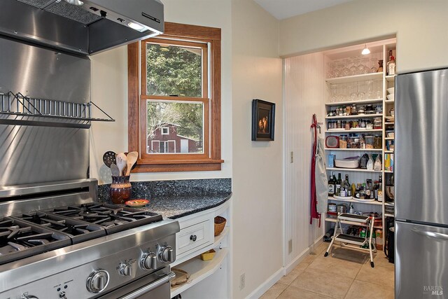 kitchen featuring dark countertops, stainless steel appliances, baseboards, light tile patterned floors, and under cabinet range hood