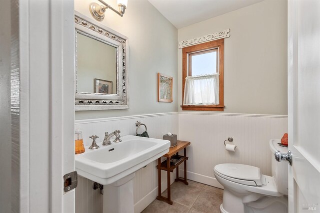 bathroom with toilet, tile patterned floors, a sink, and a wainscoted wall