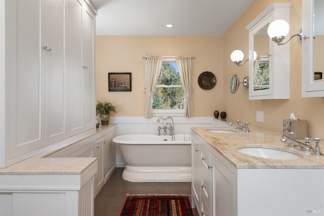 bathroom with double vanity, a sink, wainscoting, and a freestanding bath