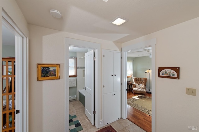 hall featuring light tile patterned floors, baseboard heating, and a wealth of natural light