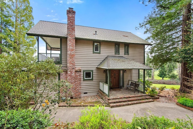 rear view of house featuring a porch, a chimney, and a shingled roof
