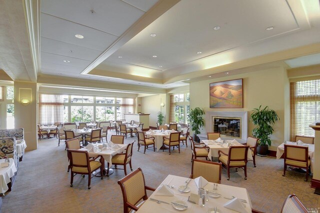 dining space featuring a raised ceiling, light carpet, and a high end fireplace