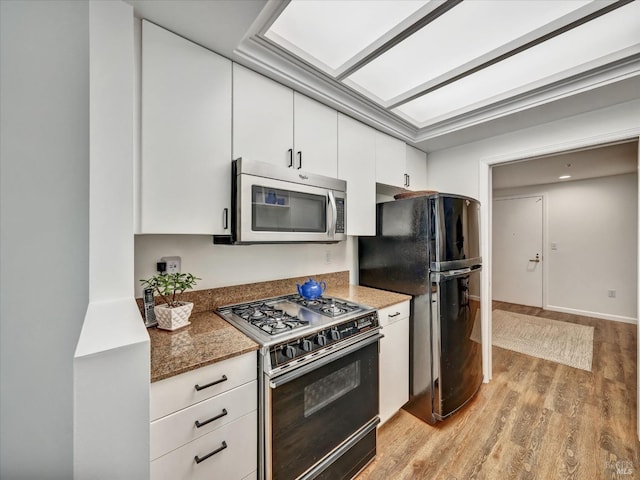 kitchen featuring stainless steel microwave, light wood-style flooring, white cabinetry, freestanding refrigerator, and gas range