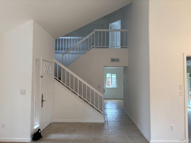 foyer entrance with a towering ceiling, tile patterned floors, visible vents, baseboards, and stairs