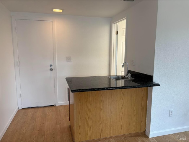 kitchen with a peninsula, wood finished floors, baseboards, and a sink