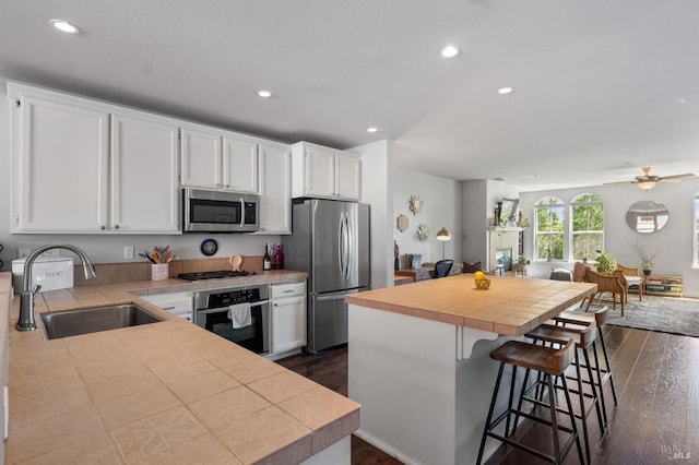 kitchen featuring a sink, tile counters, white cabinetry, appliances with stainless steel finishes, and a center island