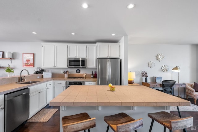 kitchen featuring recessed lighting, appliances with stainless steel finishes, white cabinetry, a sink, and a breakfast bar area
