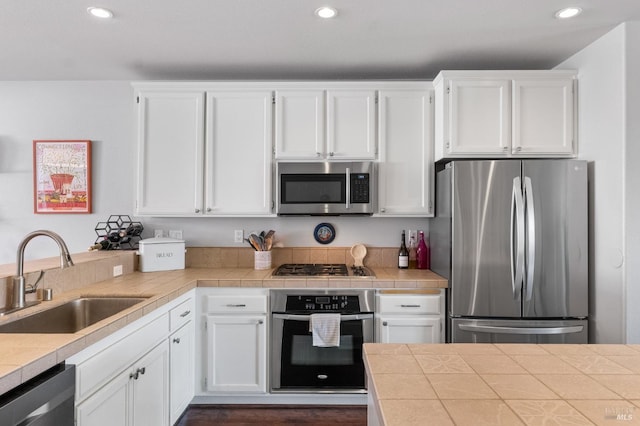 kitchen featuring white cabinetry, tile counters, recessed lighting, a sink, and appliances with stainless steel finishes