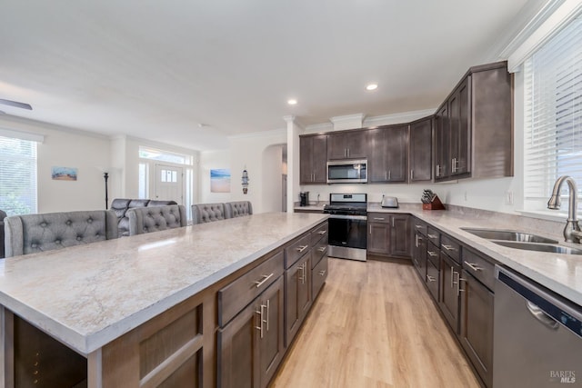 kitchen featuring a sink, a center island, stainless steel appliances, arched walkways, and dark brown cabinets