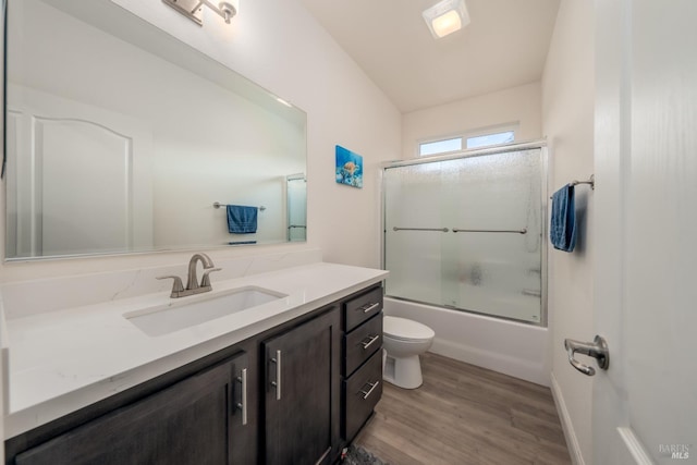 full bath with shower / bath combination with glass door, toilet, wood finished floors, and vanity