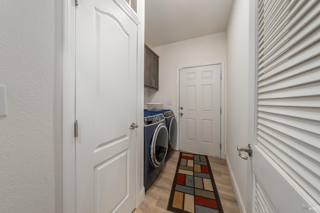clothes washing area with light wood-style flooring, cabinet space, baseboards, and washer and clothes dryer