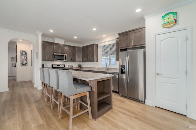 kitchen with arched walkways, dark brown cabinets, appliances with stainless steel finishes, and a center island