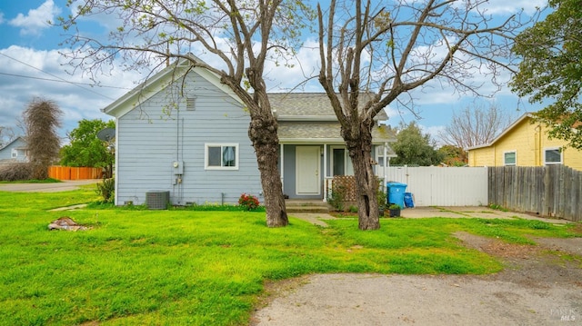 rear view of property featuring a shingled roof, fence, and a lawn