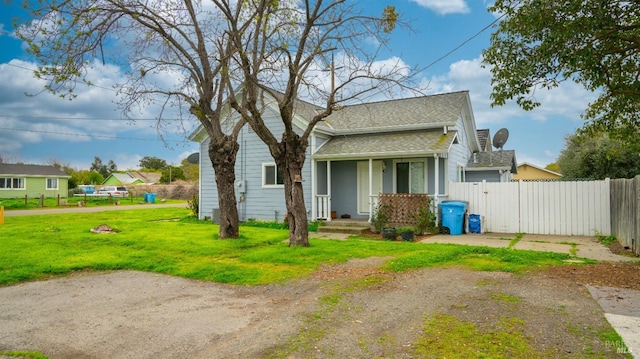 view of front facade featuring covered porch, a front yard, fence, and roof with shingles