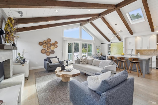 living area featuring beam ceiling, a fireplace with raised hearth, a skylight, and light wood-style floors