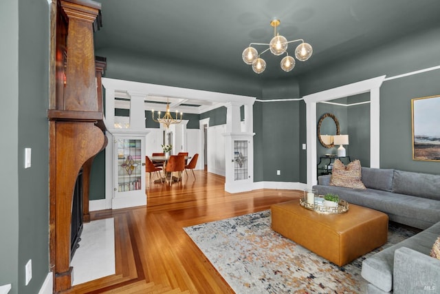 living area featuring an inviting chandelier, decorative columns, parquet flooring, and baseboards