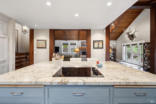 kitchen featuring black electric cooktop, open floor plan, blue cabinetry, lofted ceiling, and light stone countertops