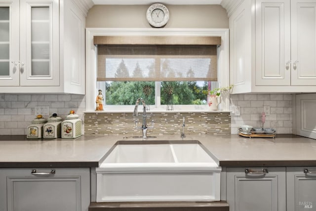 kitchen featuring white cabinetry, light countertops, decorative backsplash, a sink, and glass insert cabinets