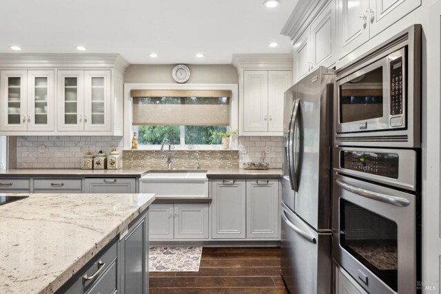 kitchen with a sink, light stone countertops, appliances with stainless steel finishes, decorative backsplash, and dark wood-style flooring