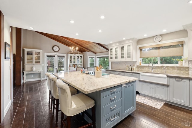 kitchen featuring decorative backsplash, white cabinets, a sink, vaulted ceiling, and a center island