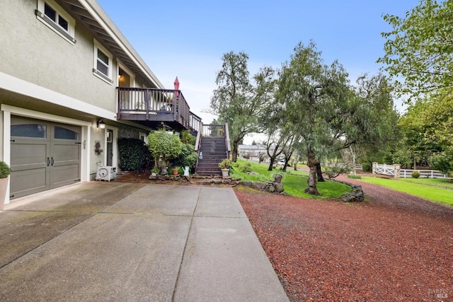 view of yard with driveway, stairs, a garage, and a deck